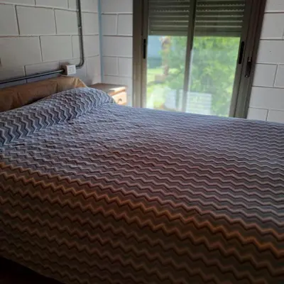 a bed with a striped comforter in front of a window at Departamento Interno, Barrio Universidad in Río Cuarto