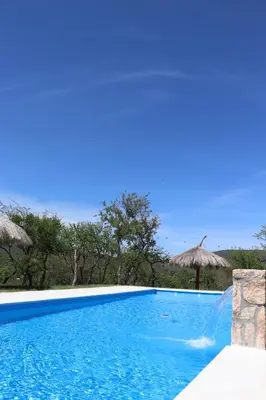a swimming pool with blue water and straw umbrellas at Refugio de las nubes in Las Rabonas