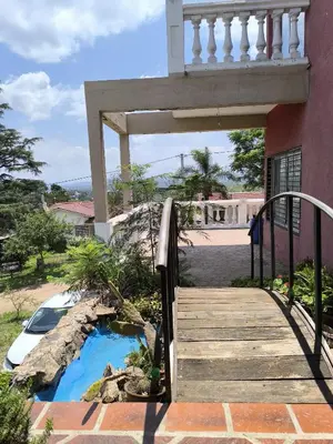 a wooden walkway leading to a house with a blue pond at Casa montaña & jacuzzi in Embalse