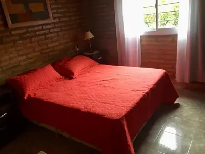 a red bed in a bedroom with a window at ovidio and Elda's house in Villa Carlos Paz