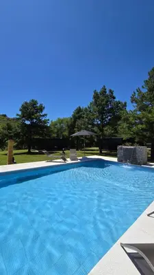 a large blue swimming pool with chairs and an umbrella at Cabañas del Campo - Solo Adultos in Atos Pampa
