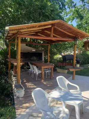 a wooden pergola with chairs and a table and a grill at Cabaña frente al balneario diquecito solo familias in Villa Carlos Paz