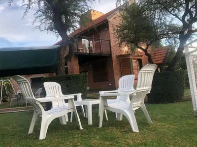 three white chairs and a table in front of a house at Cabaña Los Estribos 1 in Merlo