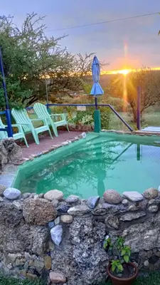 a pool with chairs and a sunset in the background at Cabaña 1 in Arroyo de Los Patos