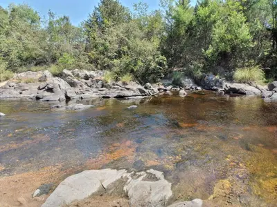 a river with rocks and trees in the background at Complejo Aguas Calmas - Casa Remanso in Los Reartes