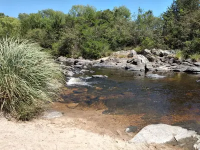 a stream of water with rocks and trees at Complejo Aguas Calmas - Casa Remanso in Los Reartes