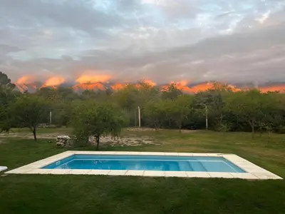 a swimming pool in a field with a fire in the background at Casa con piscina privada y vistas al Cerro Champaquí in San Javier