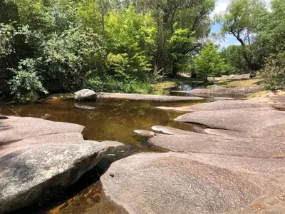 a stream of water with rocks and trees at Cabaña Tanti Estancia La Escondida in Tanti
