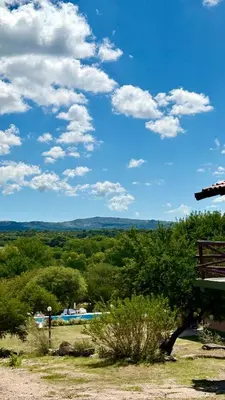 a blue sky with clouds and trees and a bench at Cabañas la posada de kika in Arroyo de Los Patos