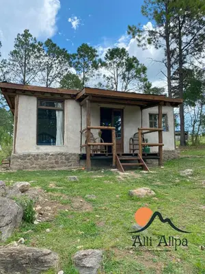 a small house with a porch and a grass field at Alli Allpa Finca y Cabañas de Montaña in Villa Yacanto