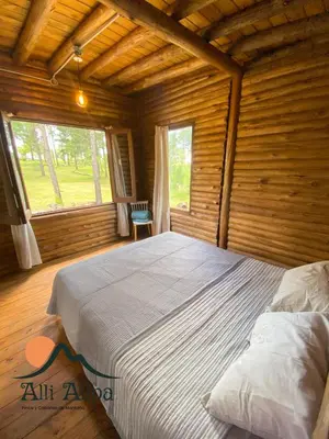 a bedroom with a large bed in a log cabin at Alli Allpa Finca y Cabañas de Montaña in Villa Yacanto