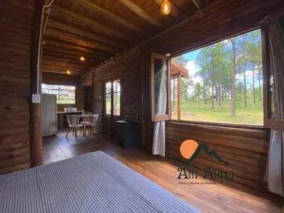 a bedroom in a log cabin with a large window at Alli Allpa Finca y Cabañas de Montaña in Villa Yacanto