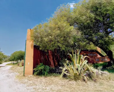 a red wall with a tree next to a dirt road at Cabaña La Abuela Chicha - Tanti in Tanti