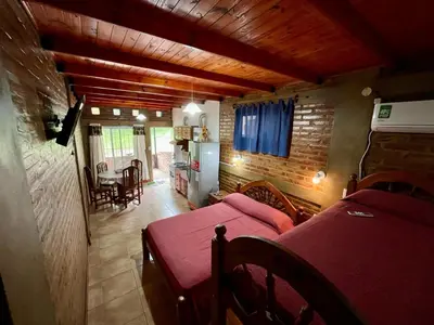 a room with two beds and a living room with a kitchen at Departamentos La Morita in Embalse