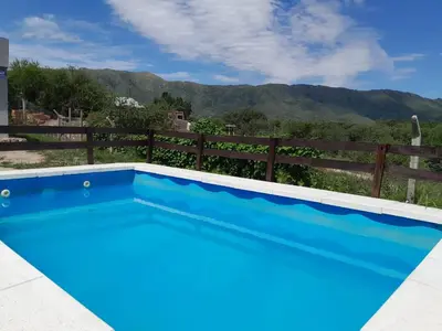 a blue swimming pool with a fence and mountains in the background at Mateo y Stella 2 in Bialet Massé