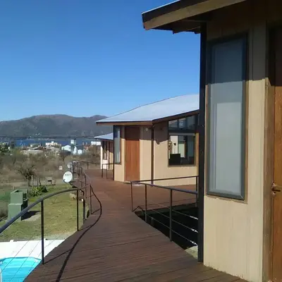 a house with a wooden walkway next to a pool at Cabañas Amanecer en Los Molinos in La Estancia