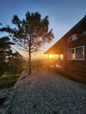 a tree next to a cabin with the sun setting at Cabaña La Lechuza in Villa Ciudad de America