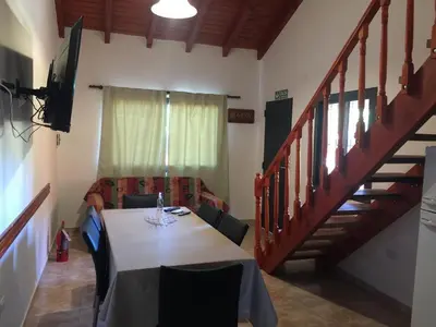 a dining room with a table and a staircase at Cabañas MAHALO in Villa Rumipal