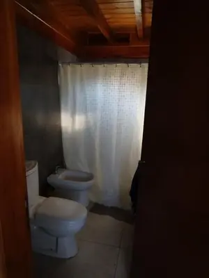 a bathroom with a toilet and a white shower curtain at Cabaña de quebracho de dos pisos in Villa General Belgrano