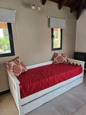 a white bed with red sheets in a room with windows at Departamento con pileta cerca del centro in Villa General Belgrano