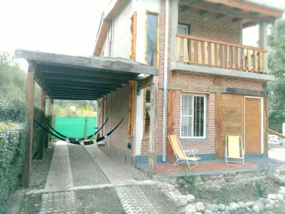 a house with a deck and a chair on a porch at CABAÑA PRIVADA NALÚ 2, Villa Ciudad Parque a 150m Río Los Reartes in Villa Ciudad Parque