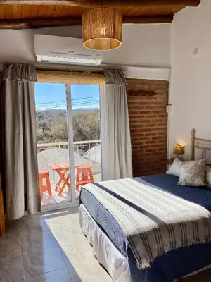 a bedroom with a bed and a balcony with a table at Clomplejo MUNAY con piscina y parking in Villa Cura Brochero