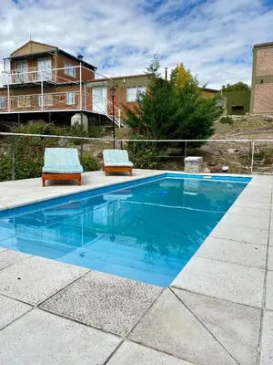 a swimming pool with two chairs and a house at Clomplejo MUNAY con piscina y parking in Villa Cura Brochero