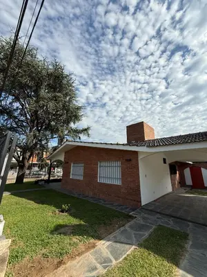 a brick house with a tree and a cloudy sky at Chalet Pino azul in Villa Carlos Paz