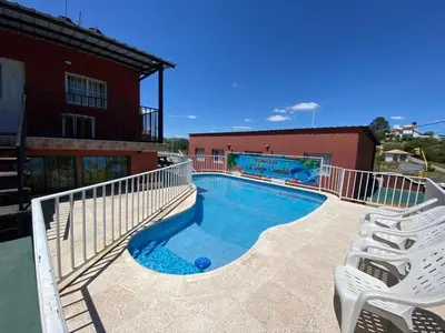 a swimming pool with two white chairs next to a building at Cabaña El Candil Solo Familias in Villa Carlos Paz