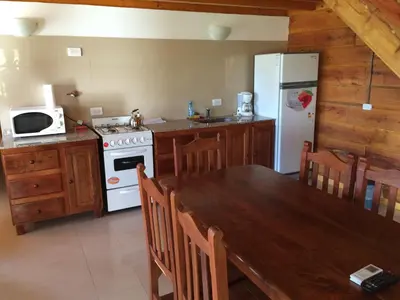 a kitchen with a table and a white refrigerator at Del Milagro Cabañas & Posada in Villa General Belgrano
