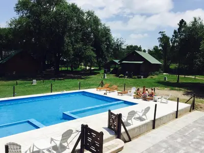 a swimming pool with people sitting in chairs around it at Del Milagro Cabañas & Posada in Villa General Belgrano
