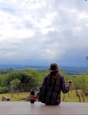 a person wearing a hat sitting on a ledge with two cups at Casa moderna y nueva, vista a las sierras con cercanía al rio in Los Reartes