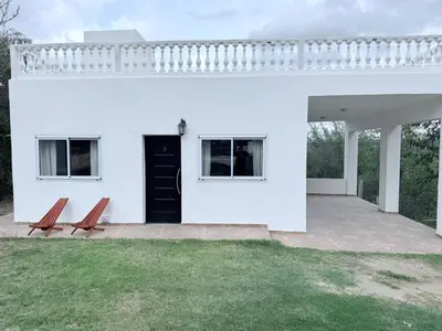 a white house with a black door and two benches at Cabañas Al atardecer in Mina Clavero