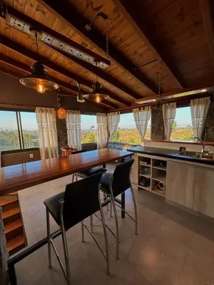 a kitchen with a long wooden bar with chairs at Cabaña Casa Flor Bru in Villa Yacanto