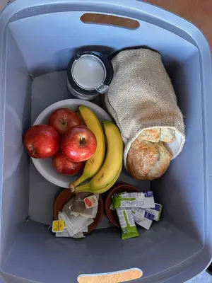 a lunch box with a bowl of apples bananas and bread at Cabañas Torres in Mina Clavero