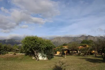 a field with a house and mountains in the background at Las Acacias Suites in Las Rabonas
