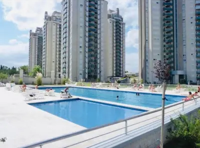 a swimming pool with people sitting on chairs and buildings at Alquiler del Departamento Barrio residencial in Cordoba