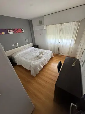a bedroom with a white bed and a wooden floor at Hotel Nuevo Uruguay in Villa Carlos Paz