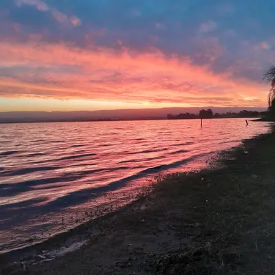 a sunset on the shore of a body of water at Ipomeas in Villa Rumipal