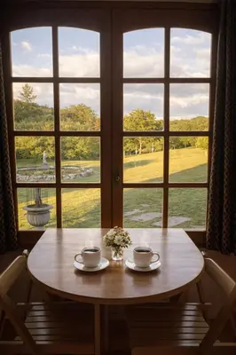 a table with two cups and flowers in front of a window at Chalet Alpino en las Sierras in Villa del Dique