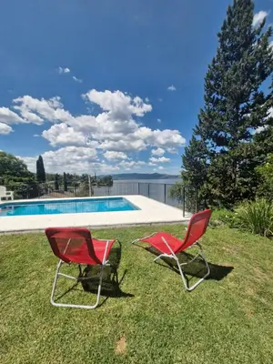 two red chairs sitting in the grass near a swimming pool at Casa con hermosa vista al lago in Villa Carlos Paz