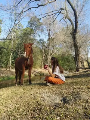 a woman sitting on the ground next to a horse at Chalet del arroyo in La Porteña