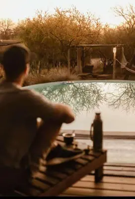 a man sitting on a bench near a body of water at Glamping Traslasierra Carpa Norte in San Javier