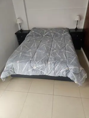 a bed with a gray comforter on top of it at Depto San Martín VCP in Villa Carlos Paz