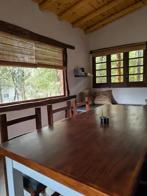 a large wooden table in a room with two windows at Cabañas Terra in Villa Yacanto