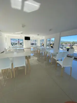 a dining room with white tables and chairs and windows at Departamento Venetto 8 in Villa Carlos Paz