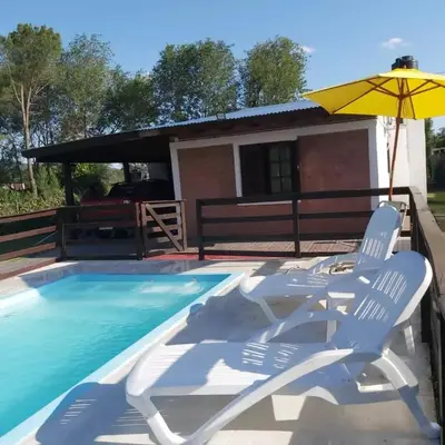 a pair of chairs and an umbrella next to a swimming pool at Cabañas Los Abuelos in Santa Rosa de Calamuchita