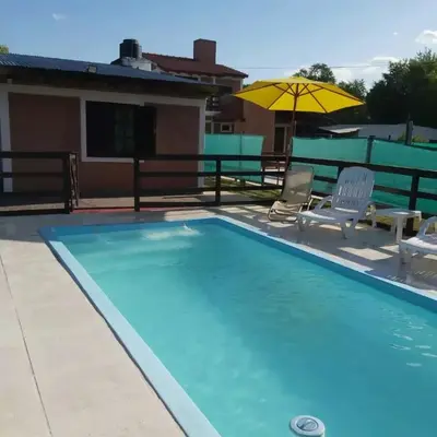 a swimming pool with two chairs and an umbrella at Cabañas Los Abuelos in Santa Rosa de Calamuchita