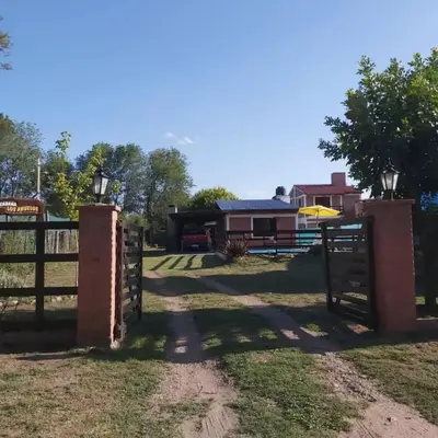 a gate to a pasture with a house in the background at Cabañas Los Abuelos in Santa Rosa de Calamuchita