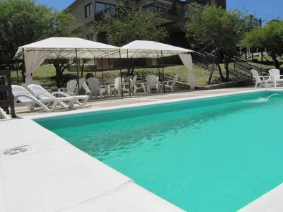 a swimming pool with white chairs and umbrellas at Cabañas El Mirador in Embalse